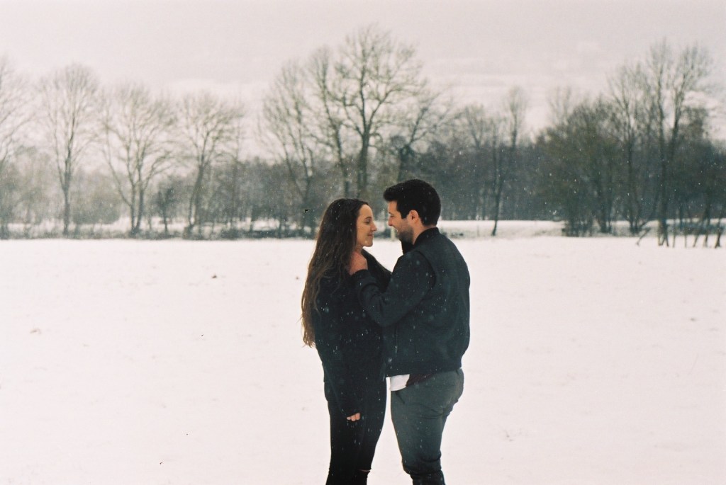 couple standing together in the snow, hands in each others face